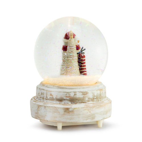 Right profile view of a lit snow globe with a rough white wood base. Inside the snow globe is a knit snowman in a red scarf and Santa hat holding a stocking next to a white tree with gold star at the top.