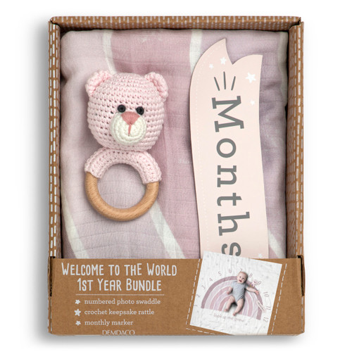 A gift set including a large light pink and white sign with the months printed on it, a light pink knit bear rattle on a wood ring and a sign that says "months", displayed in a packaging box.