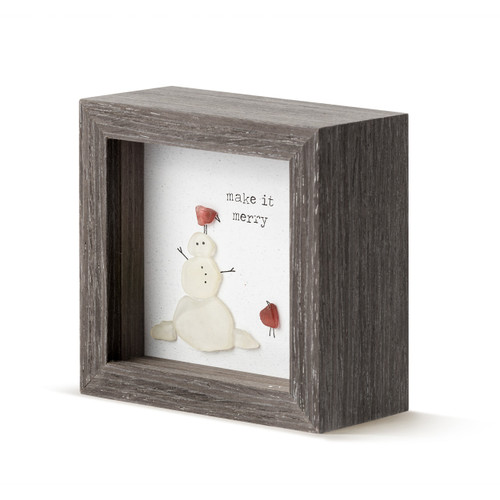 A square dark wood shadow box with a snowman and red birds and says "make it merry" made from glass pebbles, displayed angled to the left.