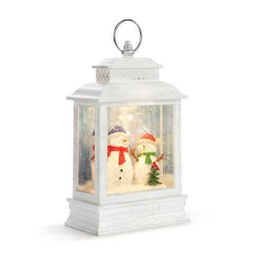 White lit lantern with two snowmen inside by a small tree with a cardinal, displayed angled to the right.