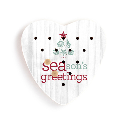 White wood heart shaped peg game that says "SEAsons greetings" with an image of a tree made of seashells. Displayed with two wood pegs in the game.
