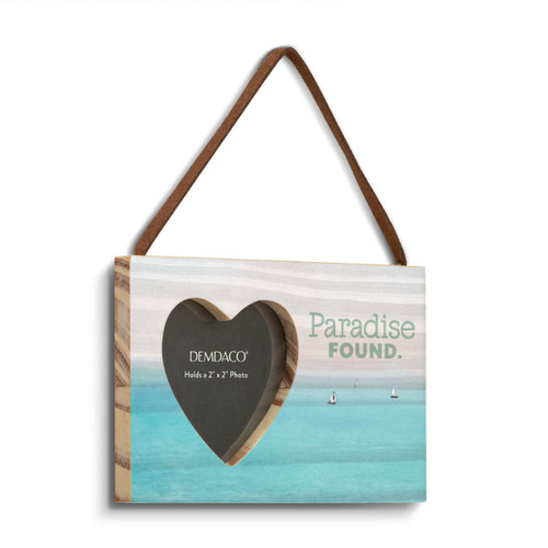 A rectangular wood hanging ornament with a 2 inch heart shaped opening for a photo with the saying "Paradise Found" next to it on a lake scene background, displayed angled to the right.