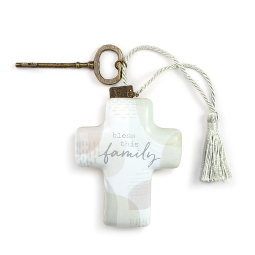 A cross shaped sculpture with a silver tassel and gold metal key attached. The cross is white and light green and says "bless this family".