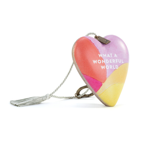 A heart shaped sculpture with a gold key and silver tassel featuring artwork created by ArtLifting artist Christina Constantine. The image is purple, yellow and orange colors  and says "What A Wonderful World", displayed angled to the right.
