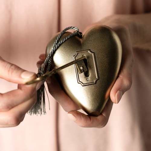 Back view of a woman holding the key partially into the lock of a heart shaped sculpture that has a gold key and tassel attached.
