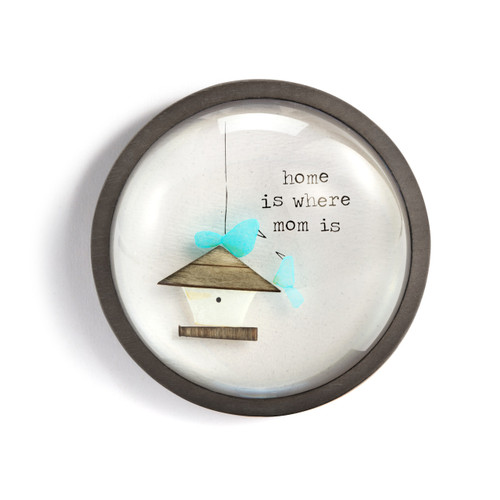 A round paperweight with a wood frame and the image of a birdhouse and two birds that says "home is where mom is".