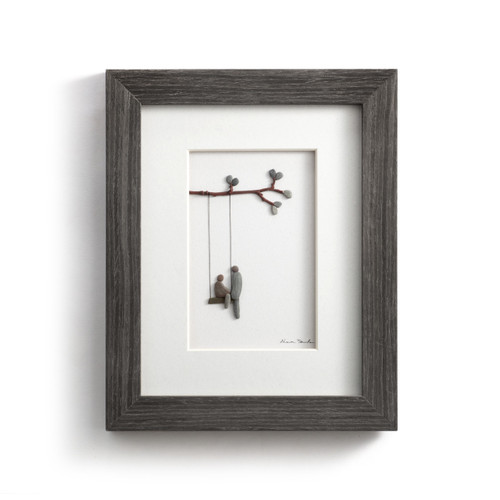 A gray wood framed image of a couple at a swing made of pebbles.