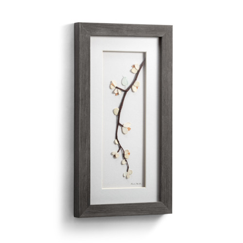 A gray wood framed image of a tree branch with a bird and flowers made of pebbles, displayed angled to the right.