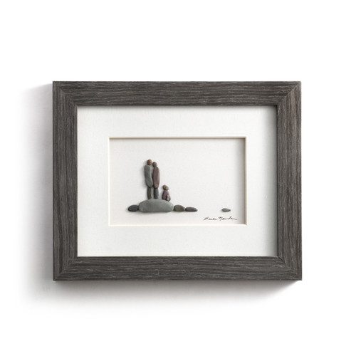 A gray wood framed image of a couple and their dog made of pebbles.