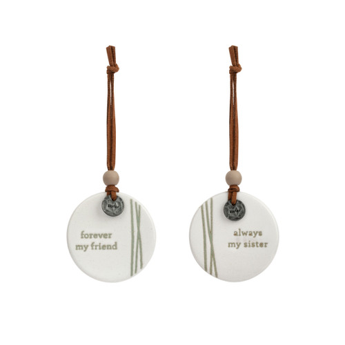 A set of two white hanging round ceramic ornaments with metal tokens that say "sister". One ornament says "forever my friend" and the other says "always my sister".