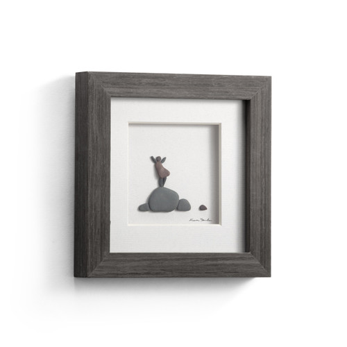 A square gray wood framed image of a happy woman made out of small pebbles, displayed angled to the right.