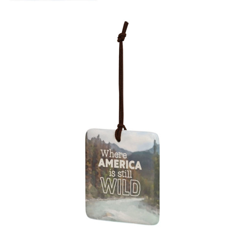 A square tile hanging ornament with a mountain stream and says "Where America is still Wild", displayed angled to the left.