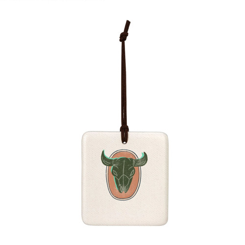 A square hanging tile ornament with a graphic image of a horned animal skull on a peach background.