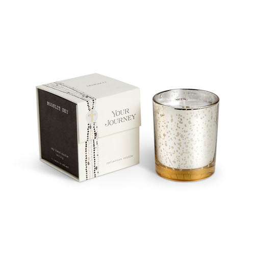 A candle in a white and gold round glass container sitting next to a black and white packaging box. The candle name is Moonlit Sky.