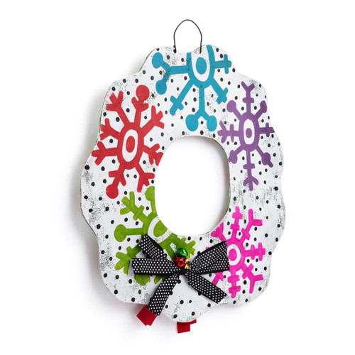 A reversible wreath shaped metal door hanger with colorful snowflakes and a black bow with small white polka dots, displayed angled to the right.