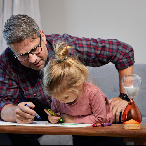 A grandfather and his granddaughter coloring together on a wood coffee table with a together time sand timer next to them.
