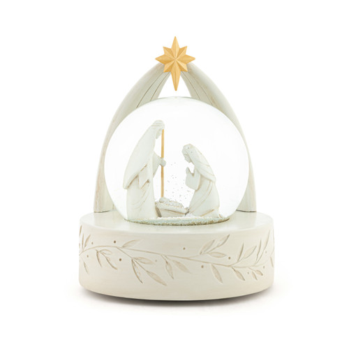 A cream ceramic snow globe with the holy family inside. There is a gold star at the top.