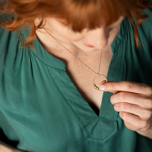 A woman wearing a gold chain necklace that has a circle charm with moving beads for a fidget.