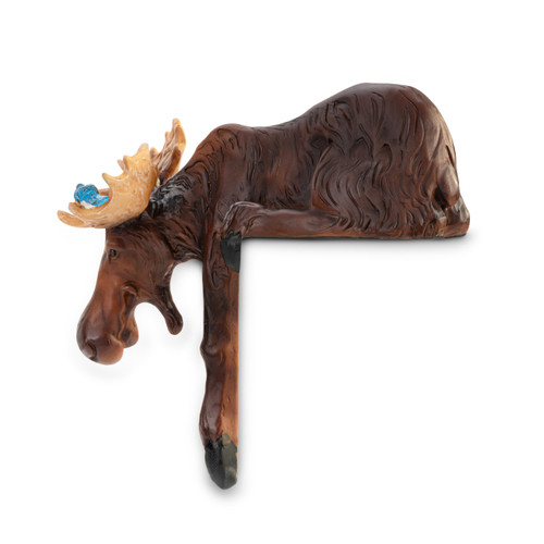Left profile view of a carved figurine of a dark brown moose with tan antlers and a small blue bird perched on them, that sits on a shelf with a front leg hanging down.