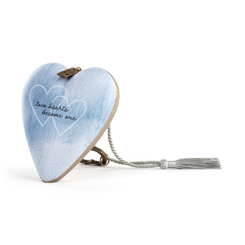 A light blue heart shaped sculpture that says "two hearts become one" with two white overlapping hearts. The heart has a silver tassel and gold key attached, displayed angled to the left.