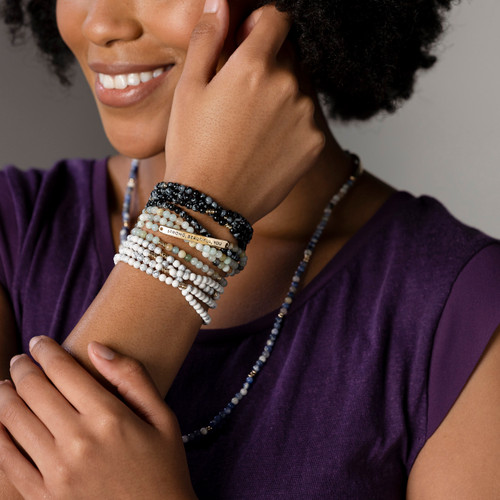 Close up of a smiling woman wearing multiple beaded bracelets on her wrist in different colors.