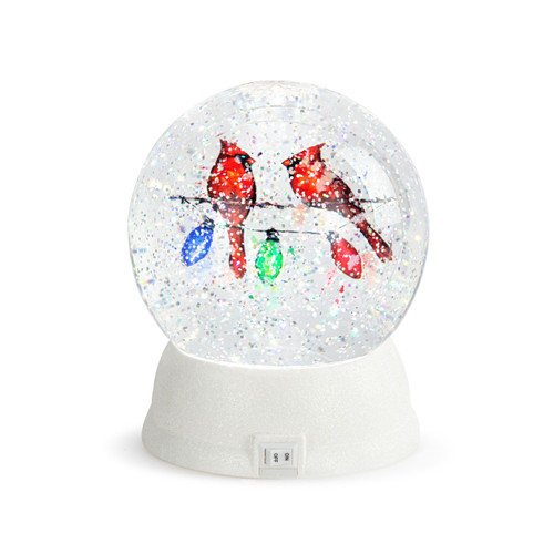 Back view of a white round glass snow globe with the image of two cardinals on a string of holiday lights.