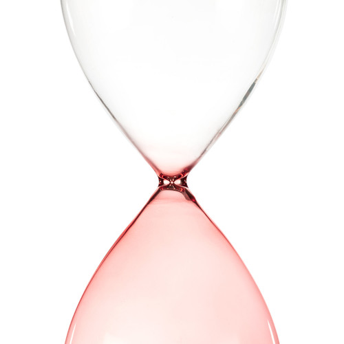 Detail view of the narrow portion of a glass sand timer with pink glass on the bottom half sitting in a wood base that reads "grandma & me time".