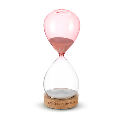 A glass sand timer with pink glass on the bottom half sitting in a wood base that reads "grandma & me time", displayed with the clear glass at the bottom and the pink on top.