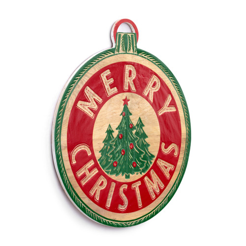 A round wood holiday door hanger with three green trees in the center and Merry Christmas in a band of red with a thin green border on the edge that looks like an ornament, displayed angled to the right.