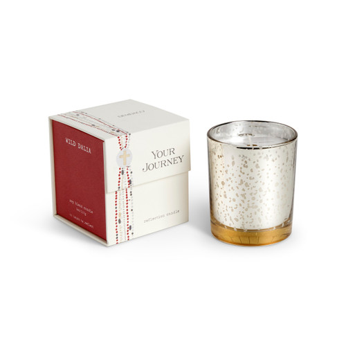 A candle in a white and gold round glass container sitting next to a red and white packaging box. The candle name is Wild Dalia.