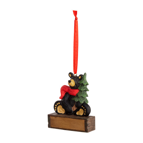 A hanging ornament with a sitting black bear in a red scarf and holding a pine tree on a rectangular base that can be personalized, displayed angled to the left.
