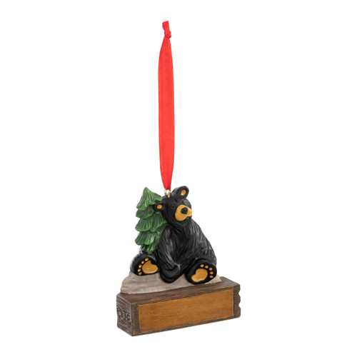 An ornament of a black bear sitting on a stone next to an evergreen tree, hanging from a red ribbon. There is a spot in front for customization, displayed angled to the right.