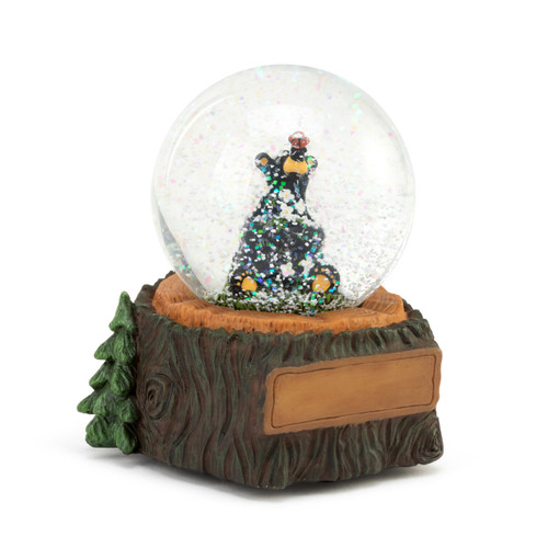 A musical snow globe with a black bear figurine holding white flowers sitting inside. The base looks like a wood tree stump with a place for customization, displayed angled to the right highlighting an evergreen tree on the left side of the base.