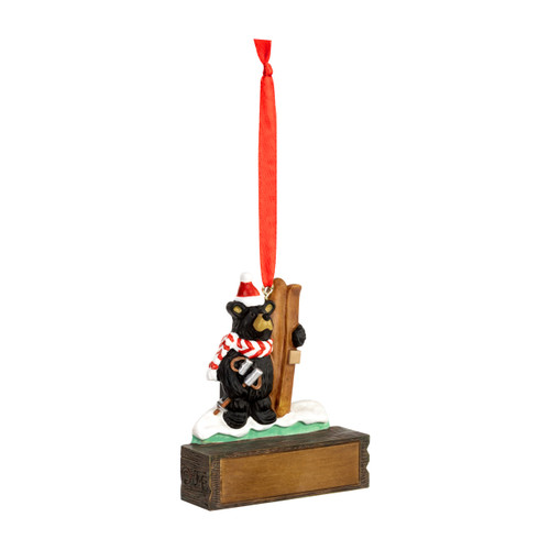 A hanging ornament with a black bear in a Santa hat and scarf holding skis on a rectangular base that can be personalized, displayed angled to the right.
