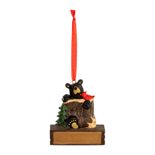A hanging ornament with a black bear in a tree trunk with a red bird on a rectangular base that can be personalized.