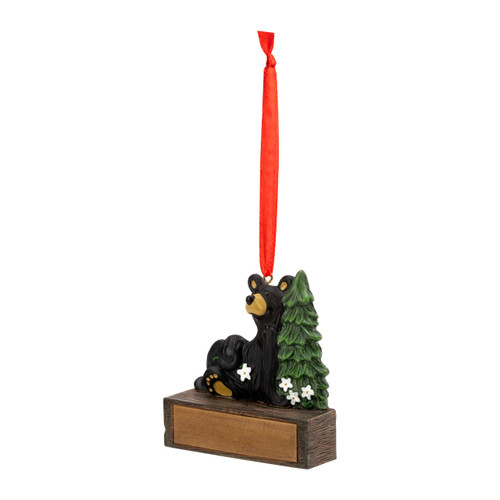 A hanging ornament with a black bear sitting by a pine tree on a rectangular base that can be personalized, displayed angled to the left.