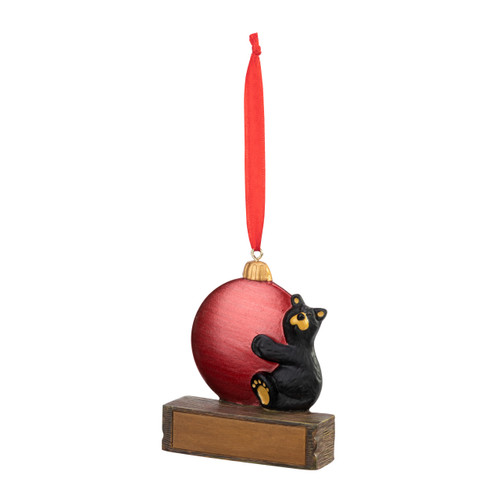 An ornament of a black bear hugging a large red ornament, hanging from a red ribbon. There is a spot in front for customization, displayed angled to the left.