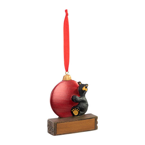 An ornament of a black bear hugging a large red ornament, hanging from a red ribbon. There is a spot in front for customization, displayed angled to the right.