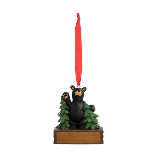An ornament of a black bear waving while standing between two trees, hanging from a red ribbon. There is a spot in front for customization.