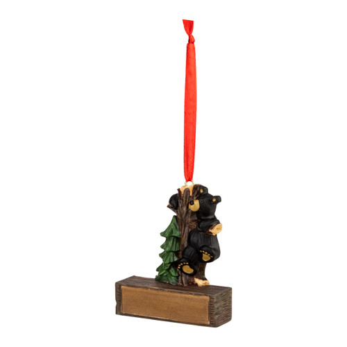 A hanging ornament with a black bear hanging onto a tree trunk on a rectangular base that can be personalized, displayed angled to the left.