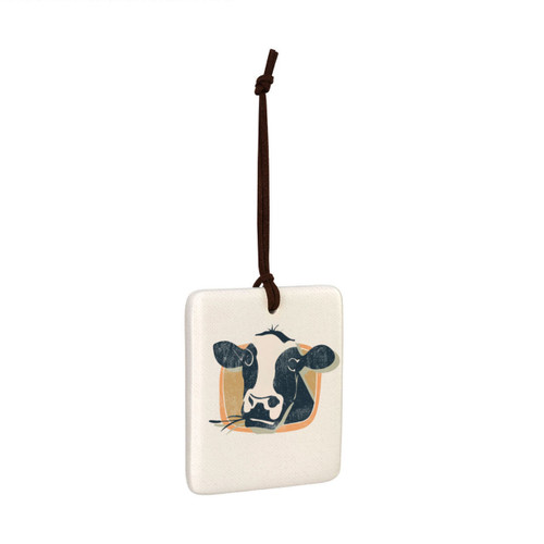 A square white tile hanging magnet ornament with a black and white cow on a tan background, displayed angled to the right.