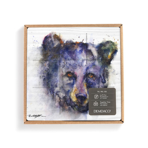 A square white wood board for tic tac toe with a watercolor image of a determined bear's face, displayed in a packaging box.