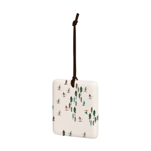 A square cream hanging tile magnet ornament with an illustration of skiers on a hillside, displayed angled to the left.