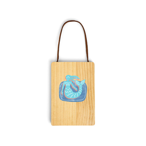 A wood hanging gift card ornament with an illustration of a light blue mermaid on a blue background on the front. The back has a holder for a gift card.