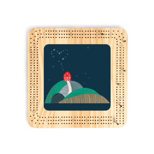 A light wood cribbage board with an illustration of a red barn on a hillside under a night sky.