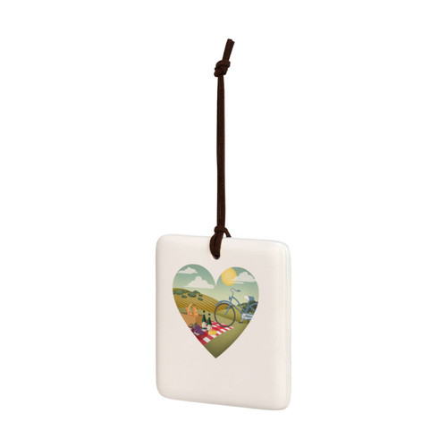 A square cream hanging tile magnet ornament with heart shaped graphic artwork of a wine and cheese picnic on a hillside, displayed angled to the left.