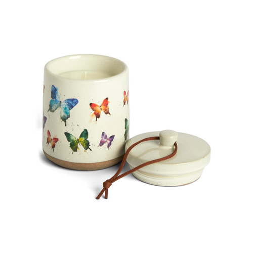 A cream ceramic candle with a tan textured base and watercolor butterflies on the outside with a removable lid, displayed off and to the side.