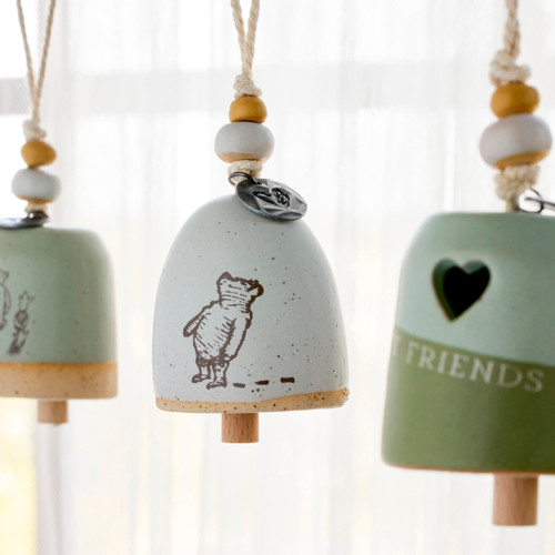 Three different cream and green Winnie-the-Pooh mini bells displayed hanging in front of a window.