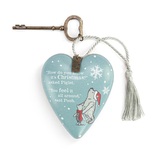 A heart shaped light blue sculpture with the image of Pooh and Piglet with a silver tassel and metal key attached. The heart says "How do you know it's Christmas?" asked Piglet. "You feel it all around," said Pooh.