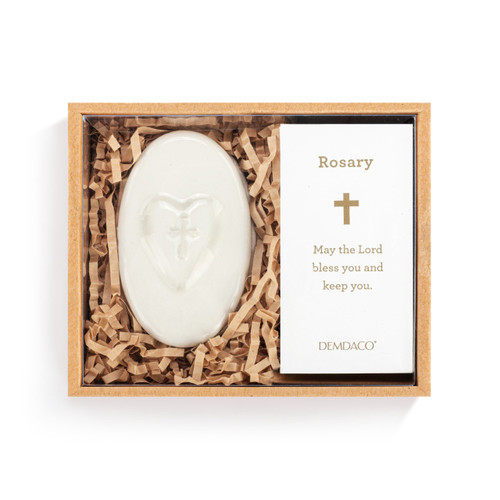An oval white ceramic trinket box next to a gold and white bead rosary, displayed in a packaging box.